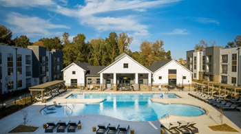 A large swimming pool surrounded by lounge chairs and buildings in the background.